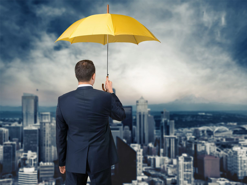 Businessman with yellow insurance umbrella looking over city
