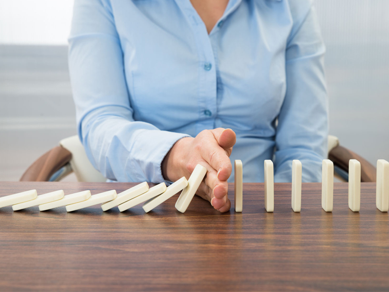 Close-up Of Businesswoman Stopping The Effect Of Domino With Hand