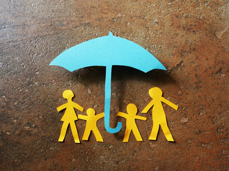 Paper family of four under a paper cutout insurance umbrella