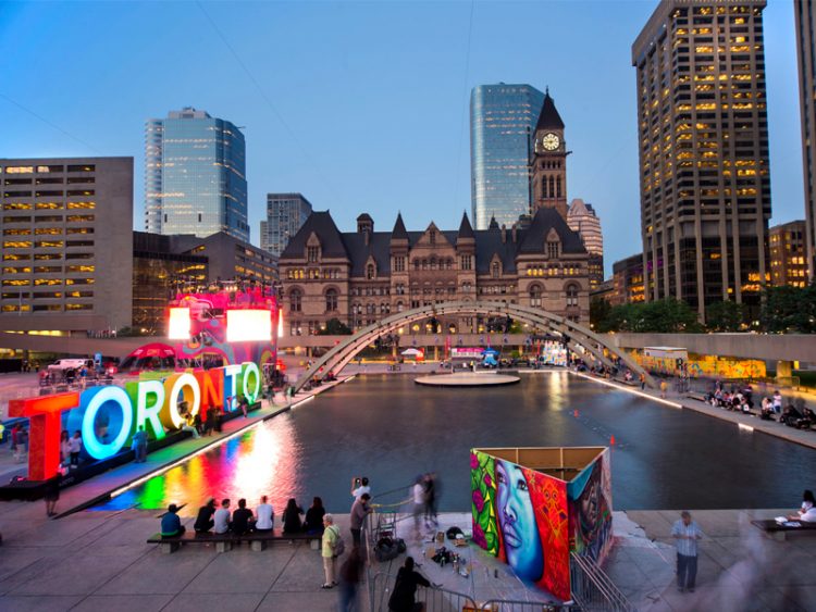 Toronto sign in Nathan Phillips Square with Old City Hall and downtown buildings in the back