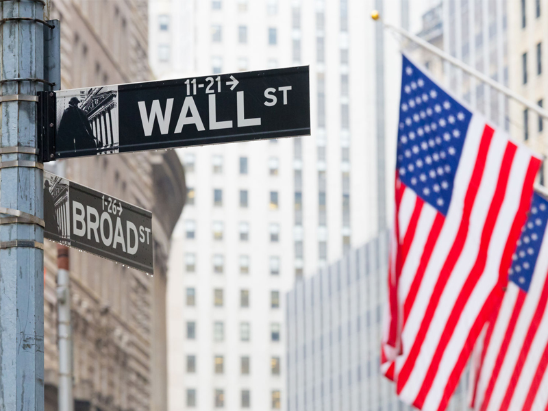 Wall street sign in New York with American flags and New York Stock Exchange background.