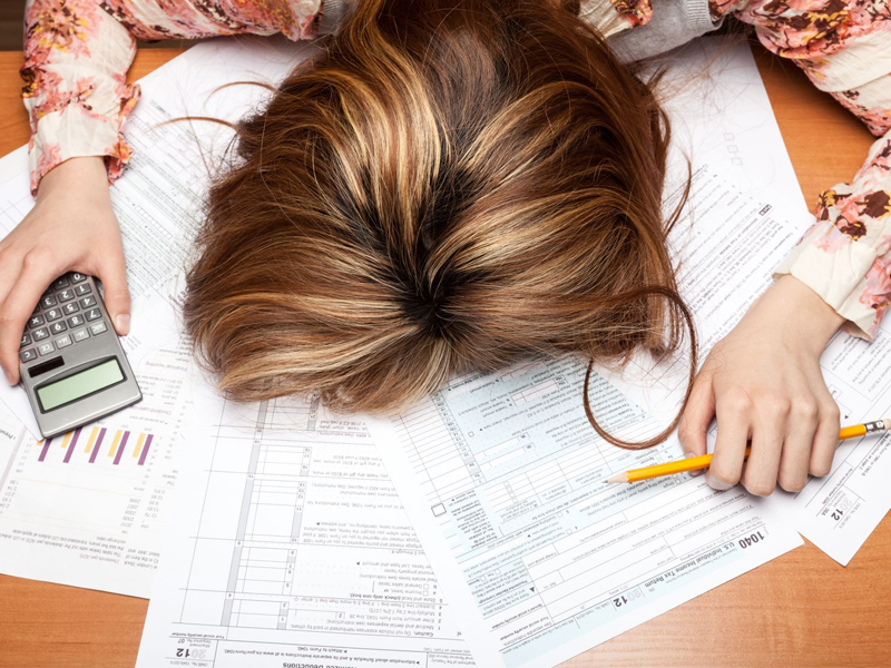 Woman face down on desk, overwhelmed by debt and calculations with calculator