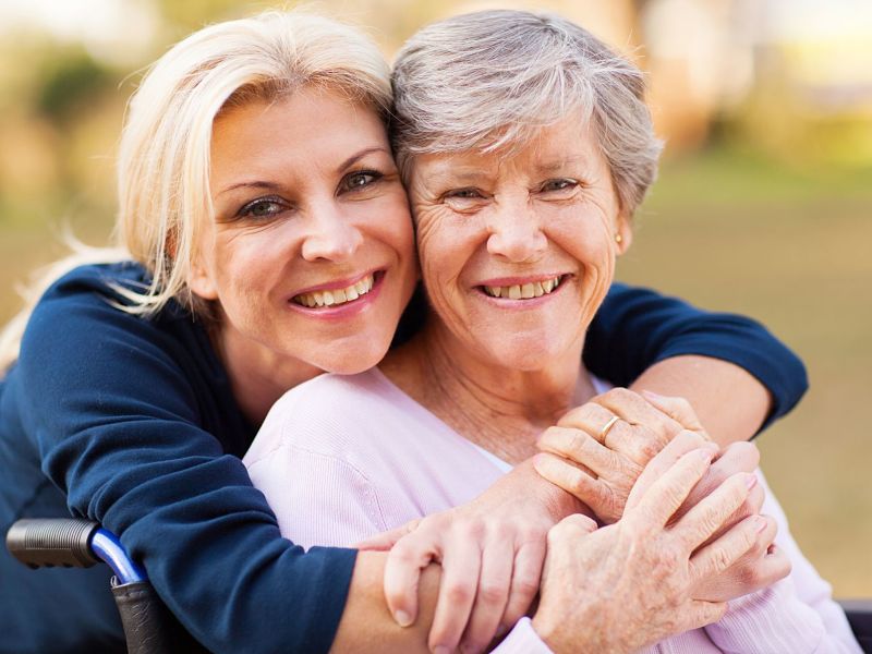 cheerful middle aged woman embracing disabled senior mother outdoors