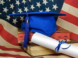 US flag, blue graduation cap and diploma on old books