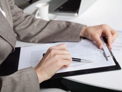 hand of a businesswoman at her desk with a pen and a clipboard