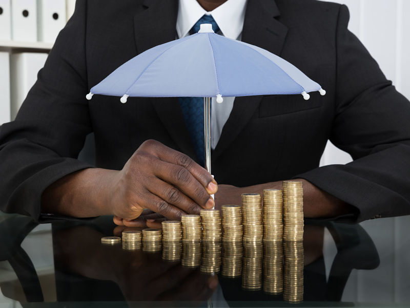 businessman protecting stack of coins with umbrella at desk