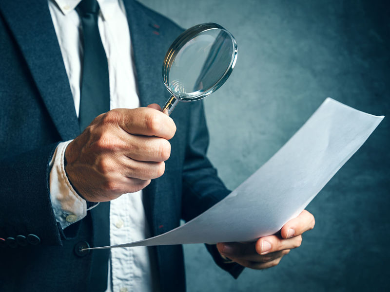 tax inspector investigating financial documents through magnifying glass, forensic accounting or financial forensics, inspecting offshore company financial papers, documents and reports.