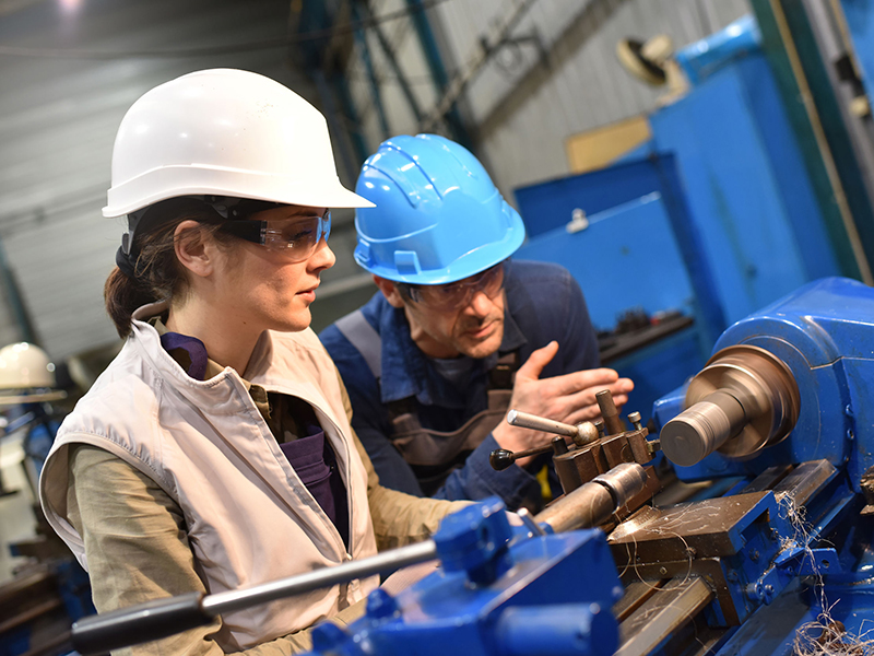 Metal worker teaching trainee on machine use