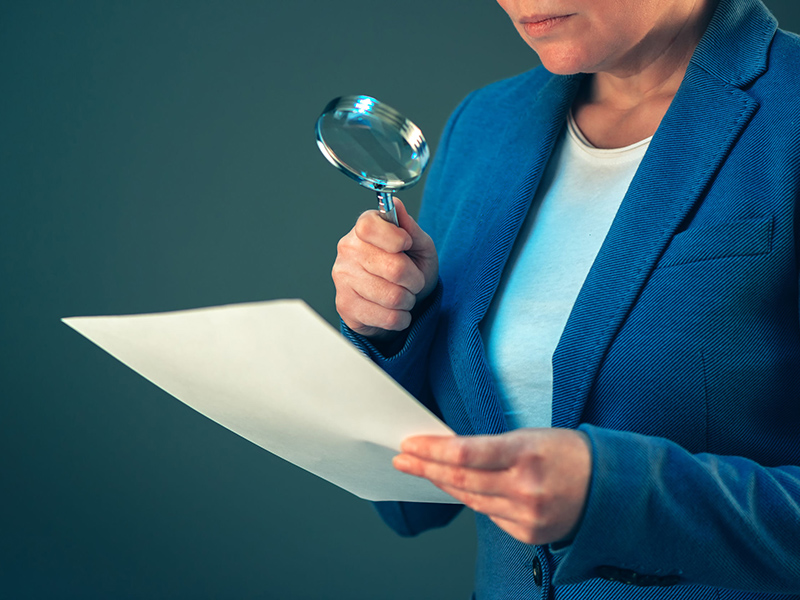 Female tax inspector looking at corporate financial documents with magnifying glass