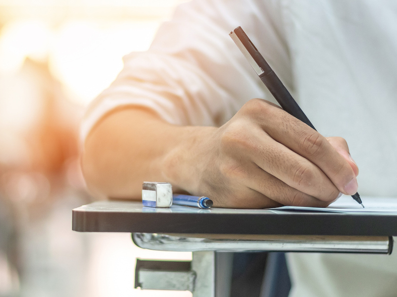 School exam student's taking educational admission test in class, thinking hard, writing answer in university classroom, education and world literacy day concept (School exam student's taking educational admission test in class, thinking hard, writing