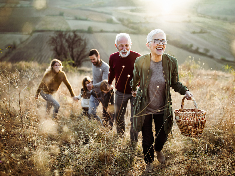 Happy mature woman holding hands with her family while moving up the hill towards their picnic place.