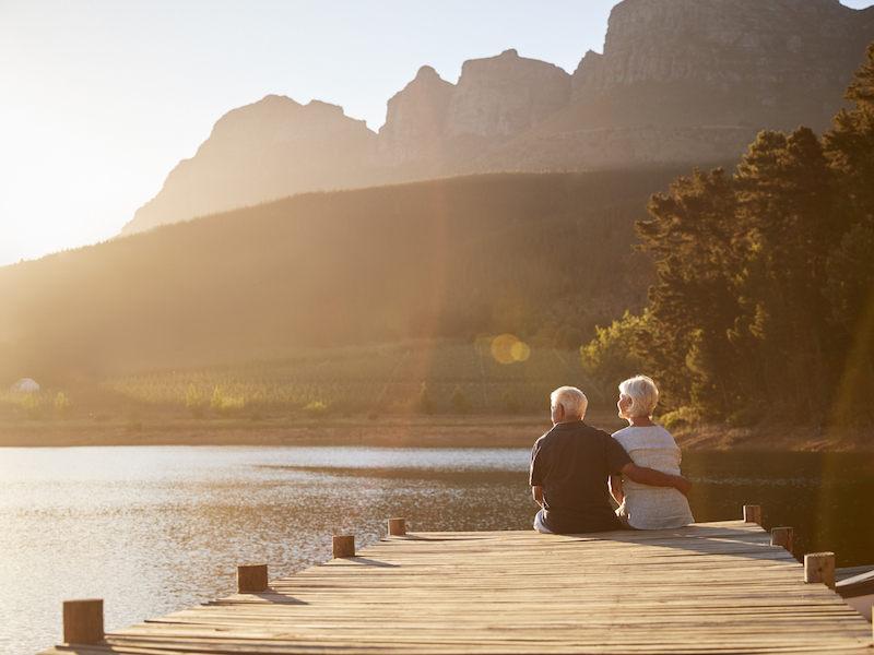 Romantic Senior Couple Sitting On Wooden Jetty By Lake