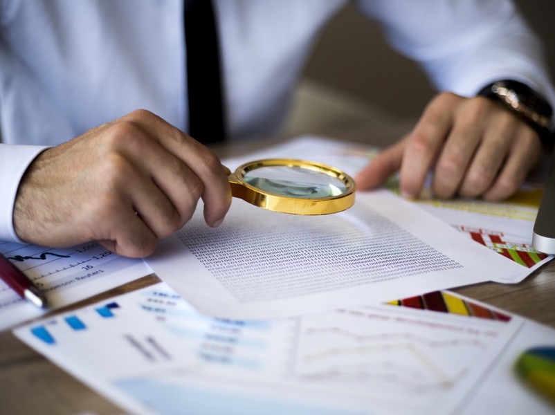 business man using magnifying glass to inspect documents