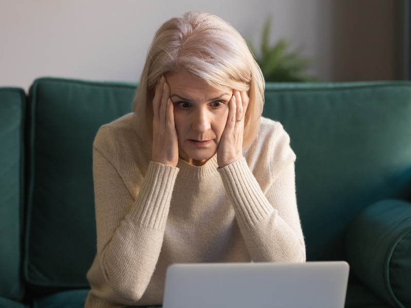 Shocked middle aged mature woman feeling stressed reading unbelievable online news, surprised senior old lady looking at laptop amazed by unexpected stuck computer problem sit on sofa at home (Shocked middle aged mature woman feeling stressed reading
