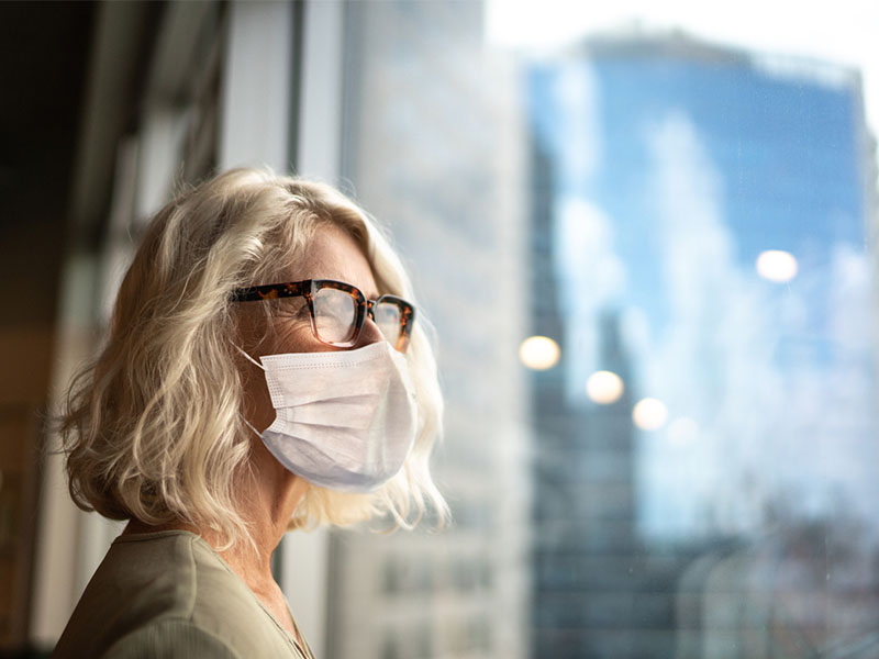 Mature businesswoman looking out of window with face mask