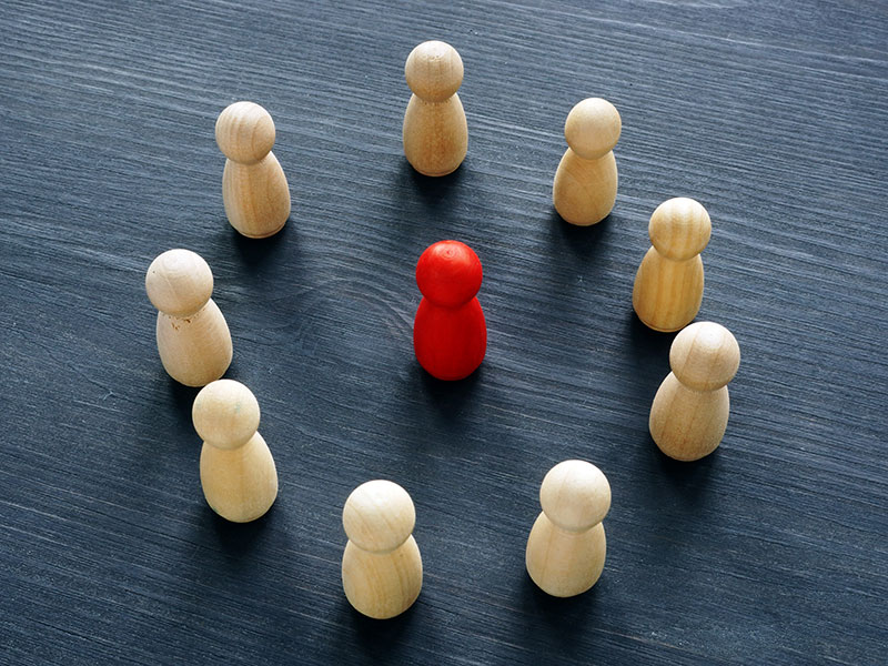 wood chess pieces surrounding red piece