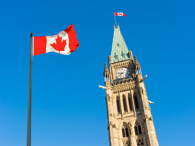Canada Parliament and Canadian Flag over blue sky.