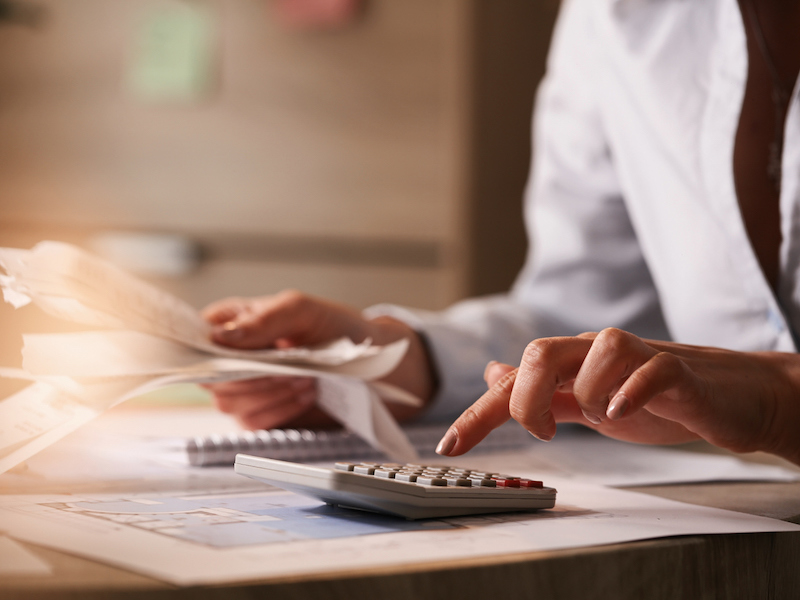 Close up of businesswoman using calculator while going through financial bills.