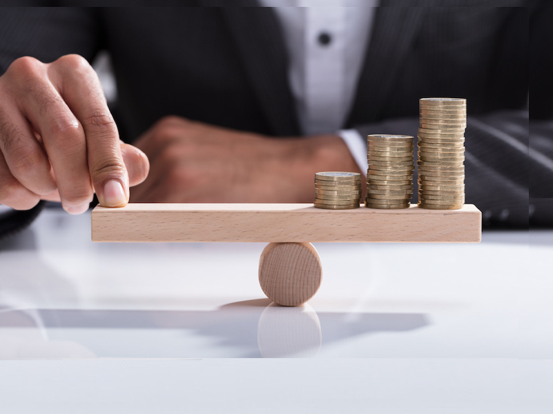 Businessperson Balancing Stacked Coins On Wooden Seesaw