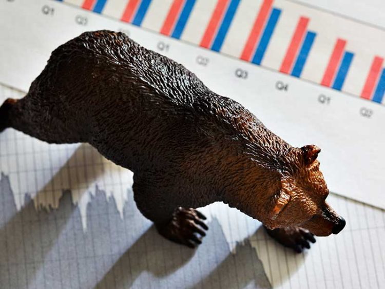 A bear rests on top of a downward pointing stock chart.