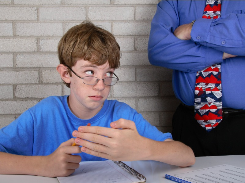 a teacher standing over a student who is hiding test answers in his hidden palm.