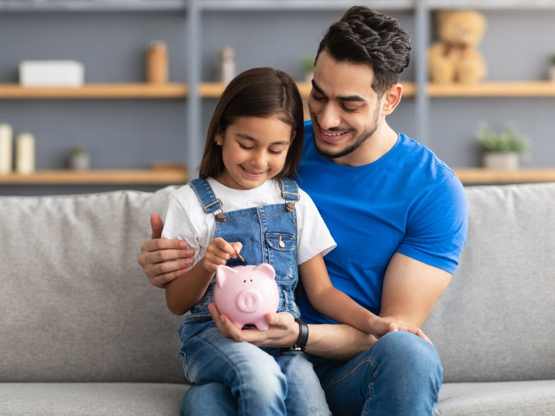 Little girl and dad saving money in piggy bank stock photo