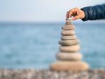 Man's hand balancing stack of stones on beach