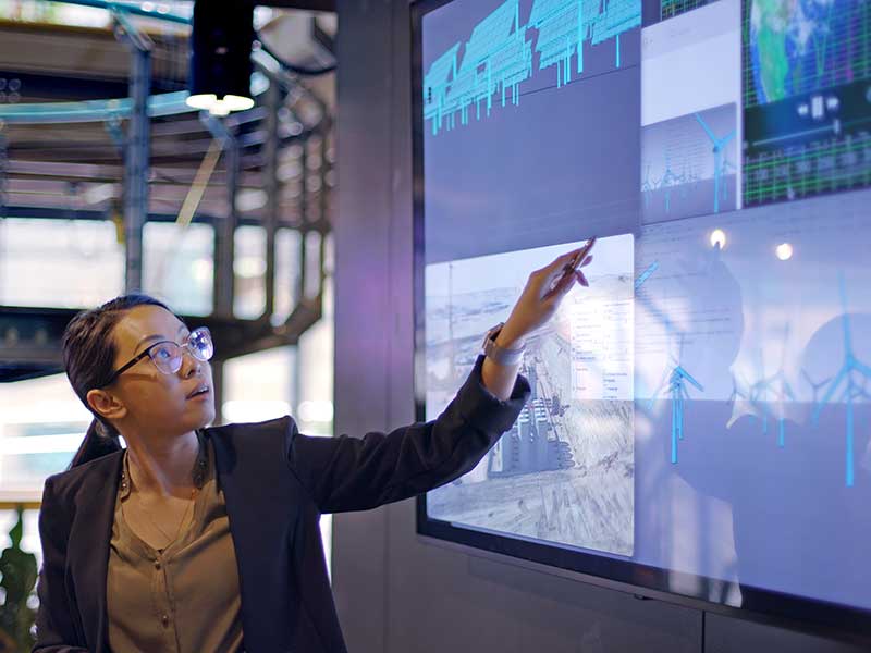 Woman pointing to wind turbines on large screen