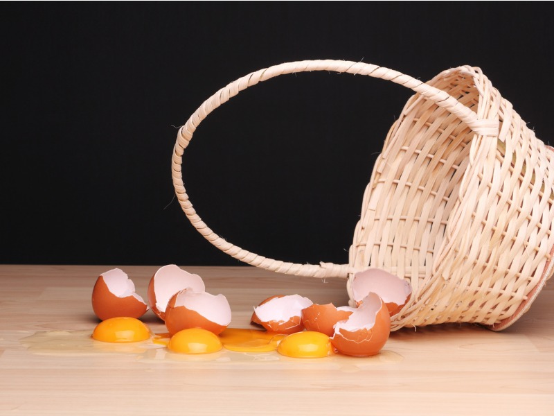 Broken eggs next to an overturned wicker basket. Concept: "Don't put all your eggs in one basket".