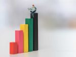 Miniature model man reading on top of bar graph of increasing value