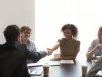 Diverse business partners gathered in boardroom shaking hands stock photo