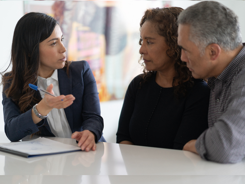 A black couple are in a meeting with their financial advisor. They are devising a financial plan to send their kids to university at their kitchen table.