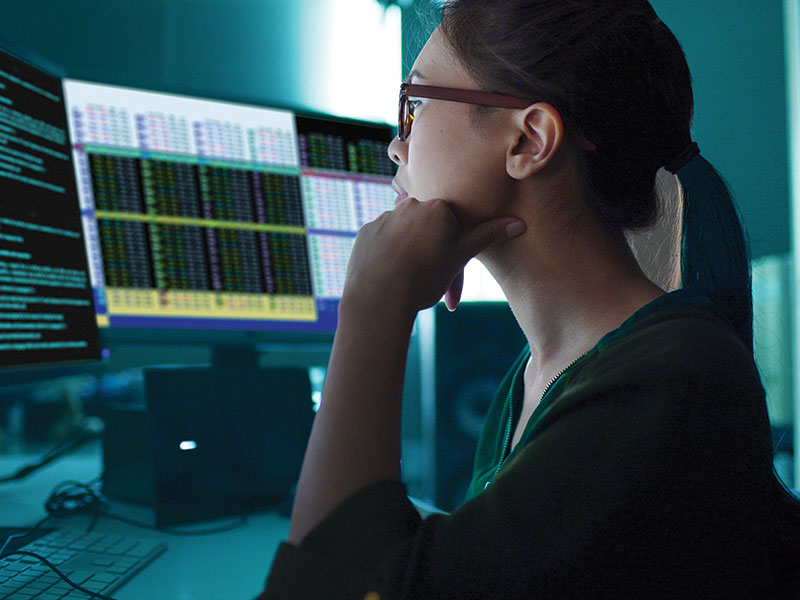 Asian woman surrounded by computer monitors in a dark room