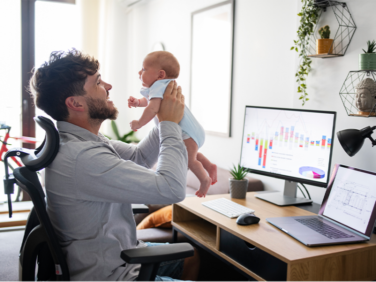 Multi-tasking father taking care of baby son while working at home office