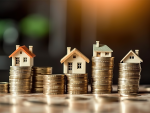 A close-up image showing several miniature houses resting on stacks of gold coins, symbolizing real estate investment, property value, or financial growth.