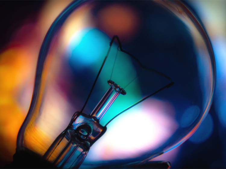 Close-up of a light bulb filament with colorful, out-of-focus lights in the background.